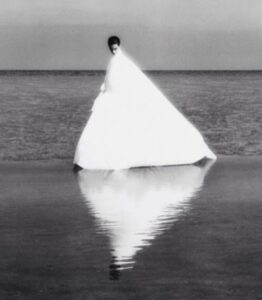 Dominique Issermann, Susan Hauser pour Parco (1985): a woman in a white triangular gown standing in the sea