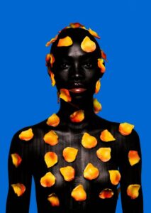 Morgan Otagburuagu, Being Black and Colourful I (2020): a woman covered in orange petals against a blue background